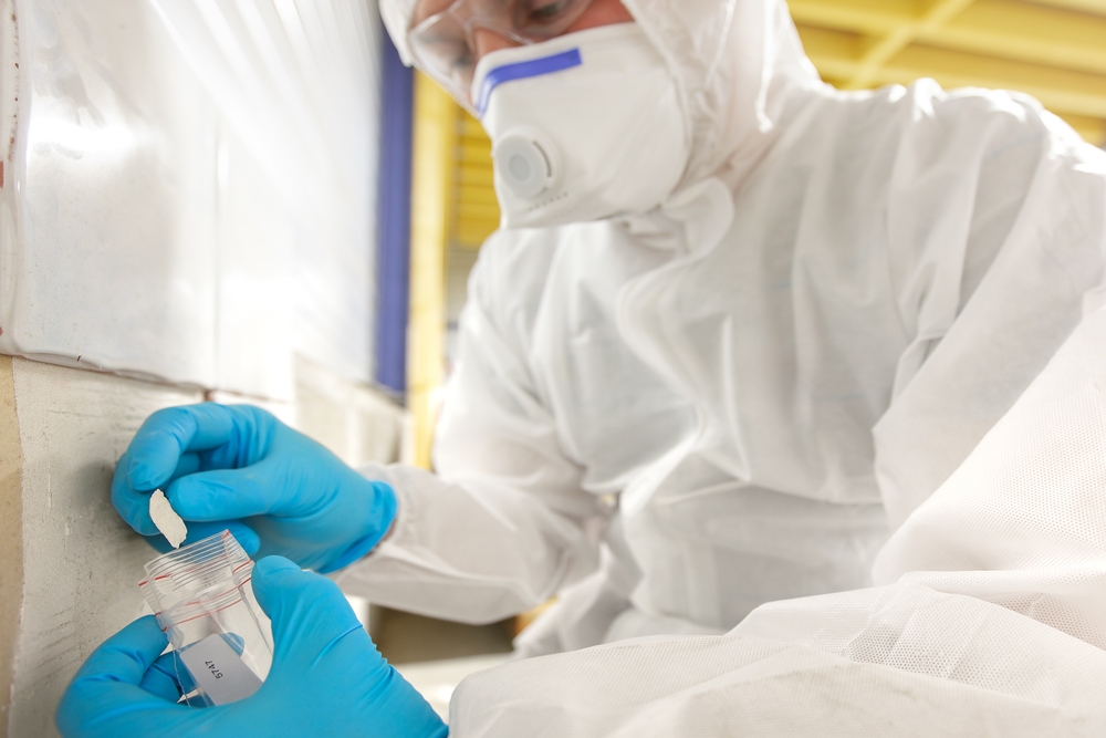Asbestos surveyor in full protective equipment bagging a sample for laboratory testing